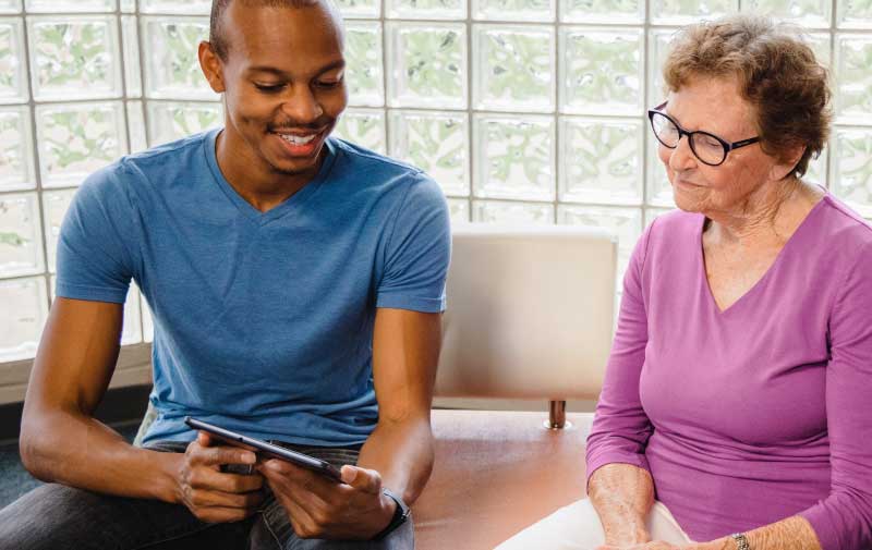 Male nurse looking at tablet with elderly woman sitting next to him